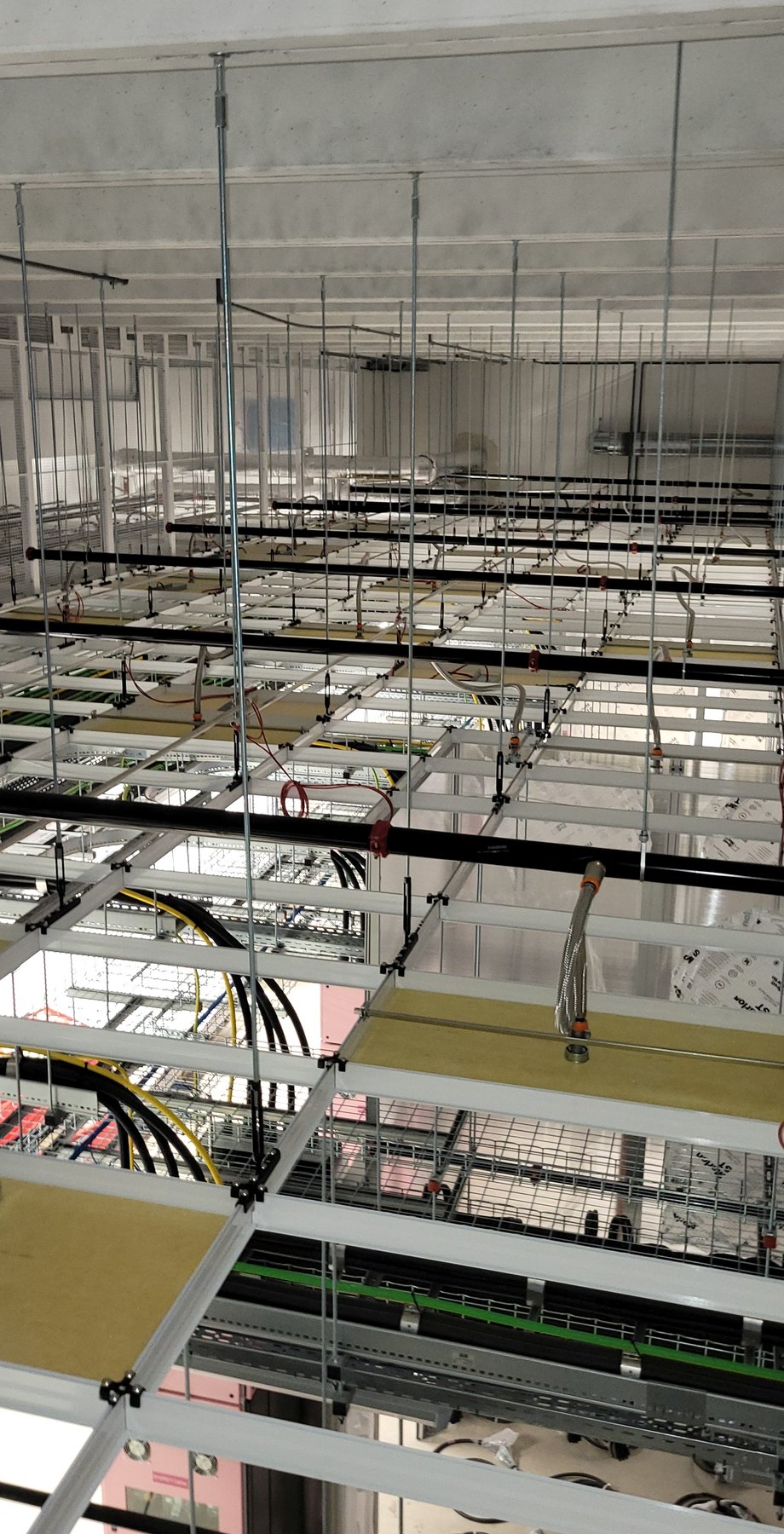 COM.SAR IT Cleaning project photograph: multiple installation levels with cable trays, pipework and support profiles in a ceiling void. COM.SAR IT Cleaning project photograph: multiple installation levels with cable trays, pipework and support profiles in a ceiling void.