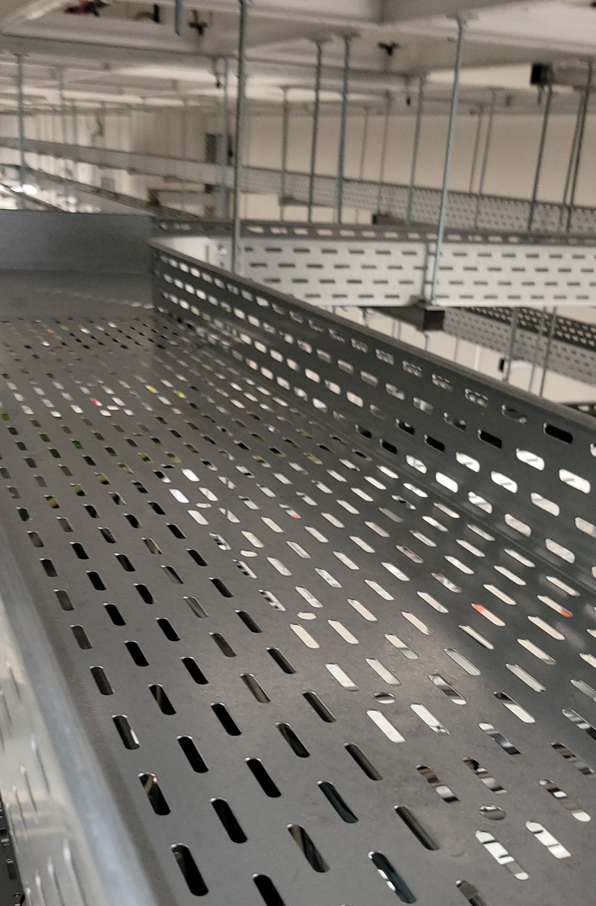 COM.SAR IT Cleaning project photograph: close-up of a perforated cable tray above the ceiling. COM.SAR IT Cleaning project photograph: close-up of a perforated cable tray above the ceiling.