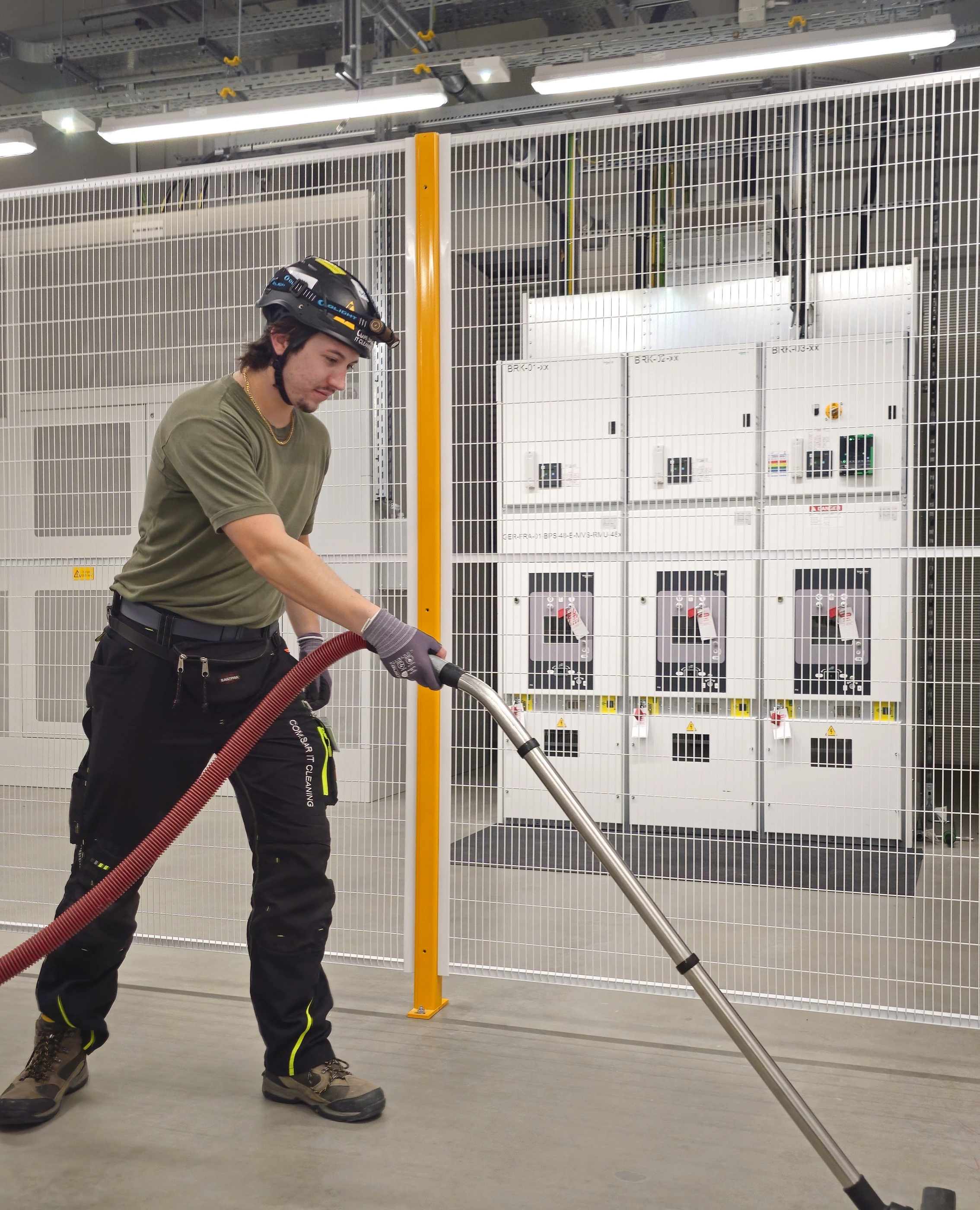 Mitarbeiter von COM.SAR IT Cleaning saugt die Bodenfläche vor einer eingehausten Anlage.