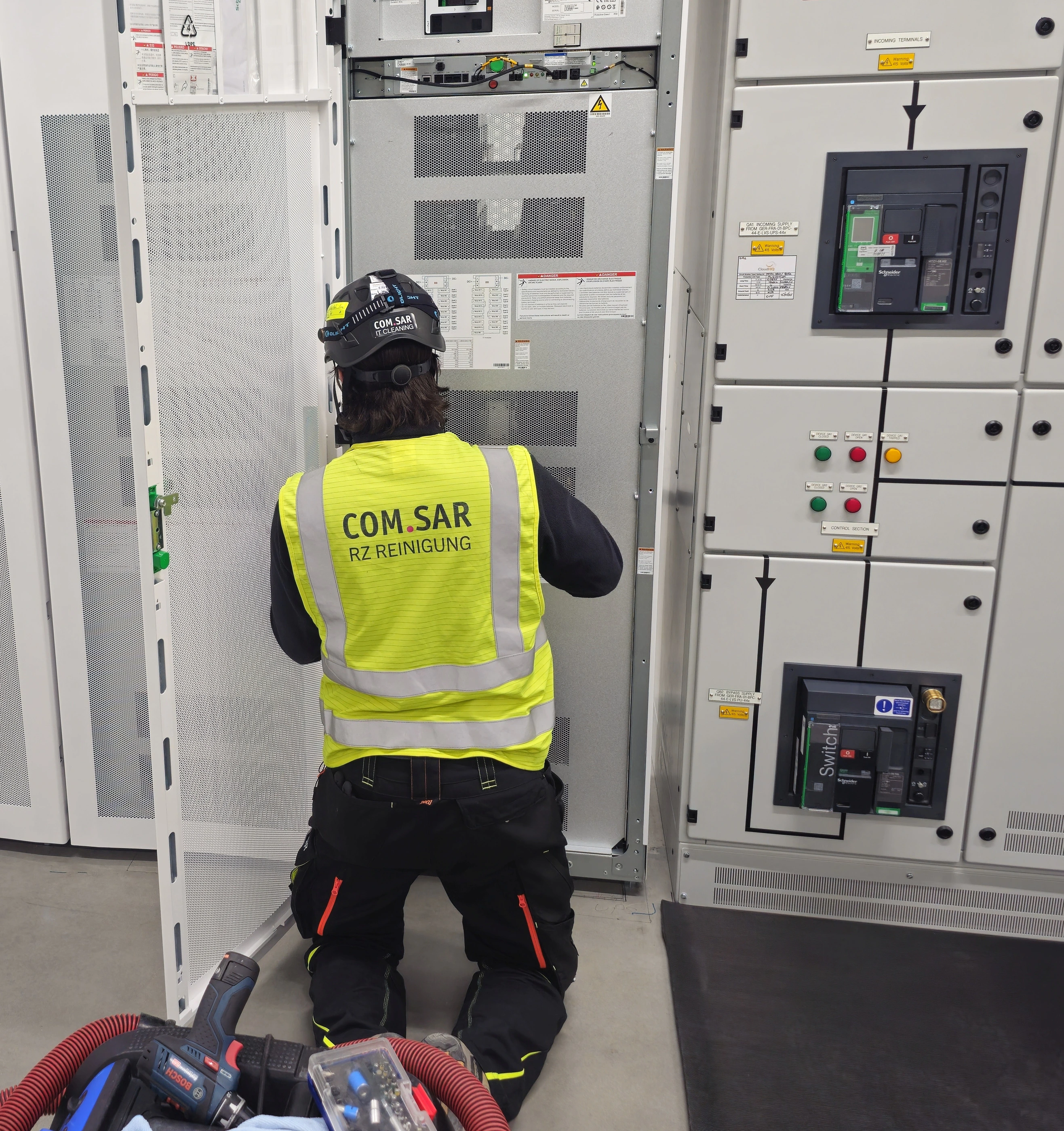 Mitarbeiter von COM.SAR IT Cleaning vor einem geöffneten Anlagenschrank.