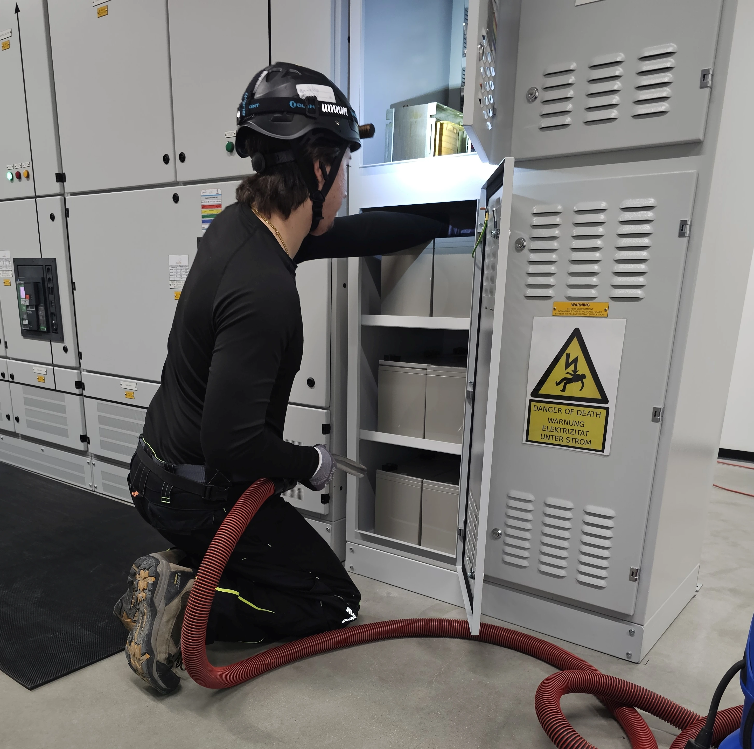 Mitarbeiter von COM.SAR IT Cleaning mit einem Reinigungsschlauch vor einem geöffneten Anlagenschrank.