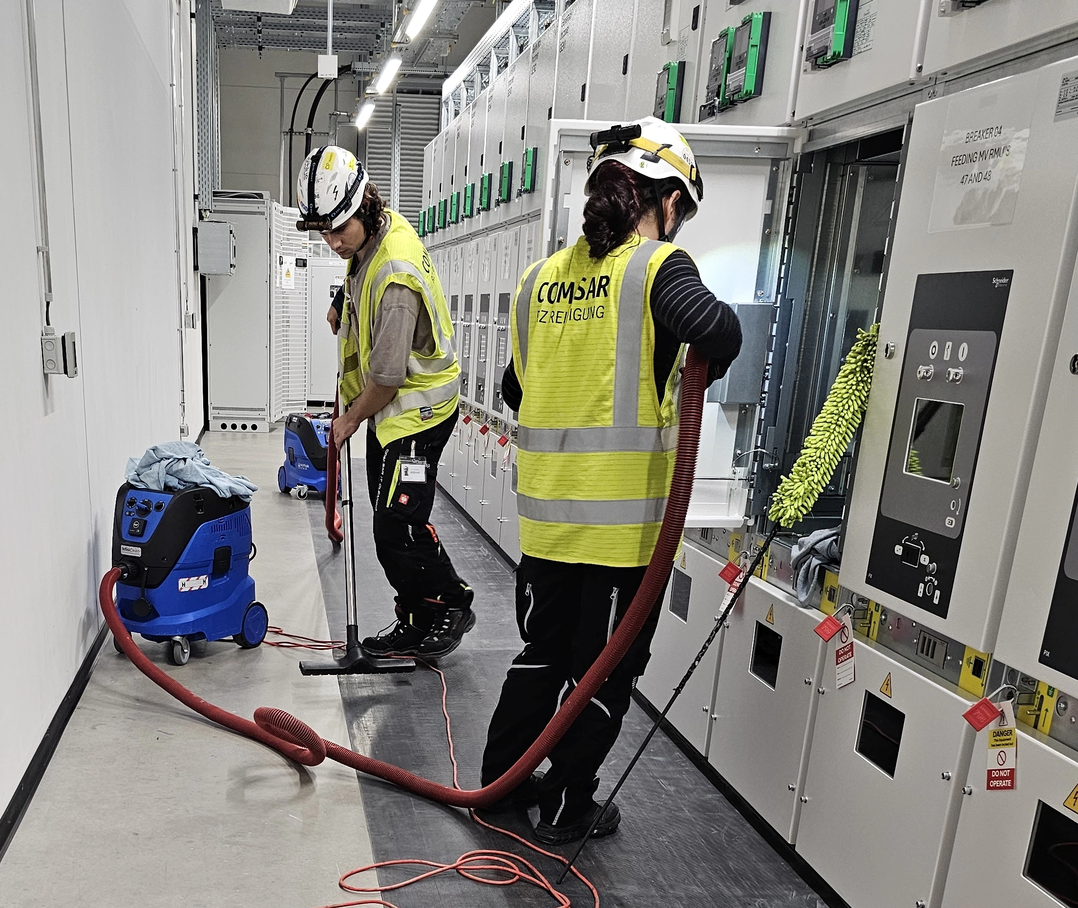 COM.SAR IT Cleaning project photograph: two team members cleaning switchgear, drawout mechanisms and floor surfaces. COM.SAR IT Cleaning project photograph: two team members cleaning switchgear, drawout mechanisms and floor surfaces.