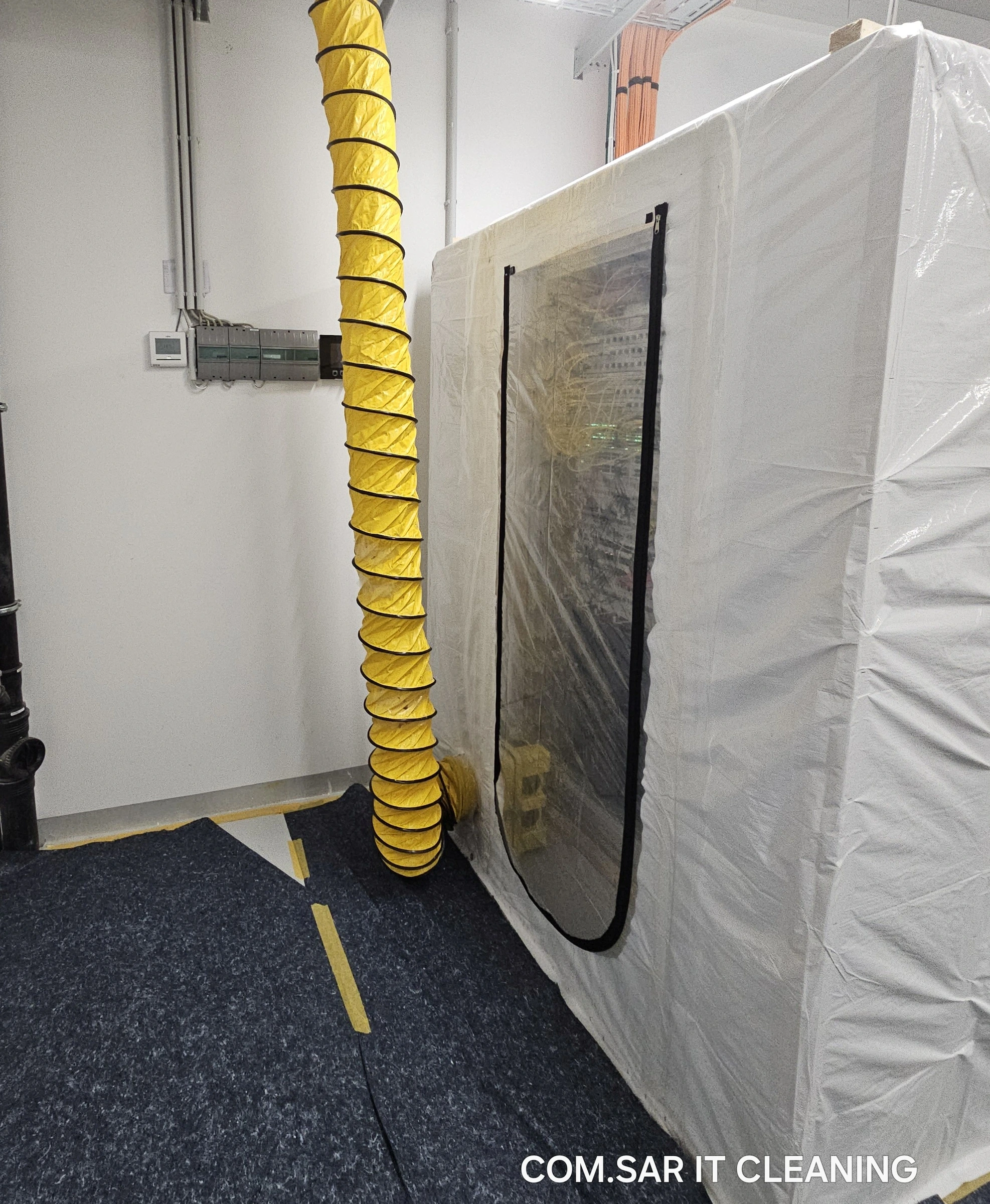 Network cabinet enclosed in plastic sheeting with zipped access and a flexible yellow air duct.