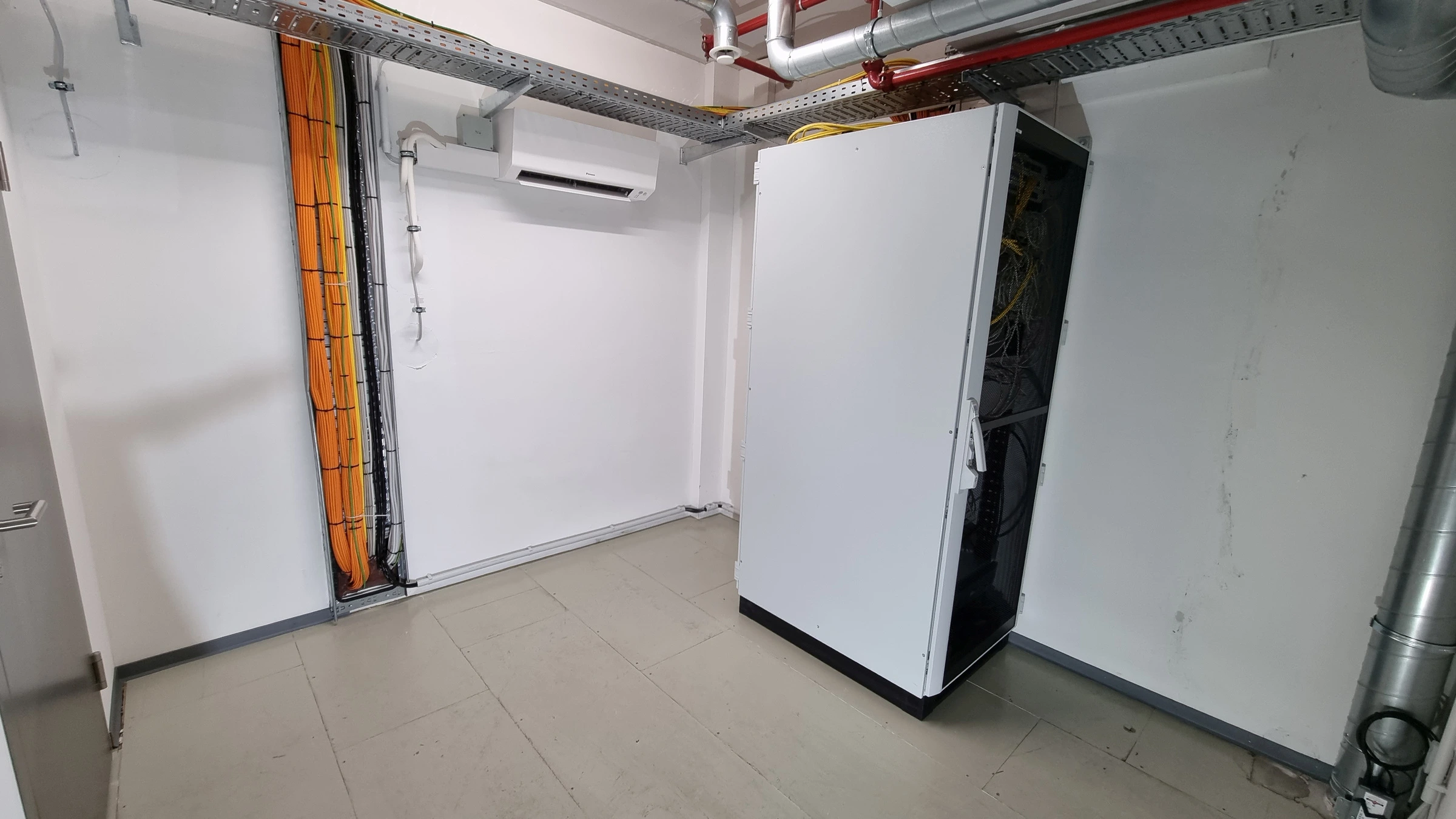Patchraum mit Netzwerkschrank, Kabeltrassen, vertikaler Verkabelung und Wandklimagerät.